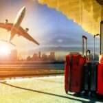 Avião a descolar de um aeroporto ao pôr do sol, com duas malas de viagem vermelhas em primeiro plano